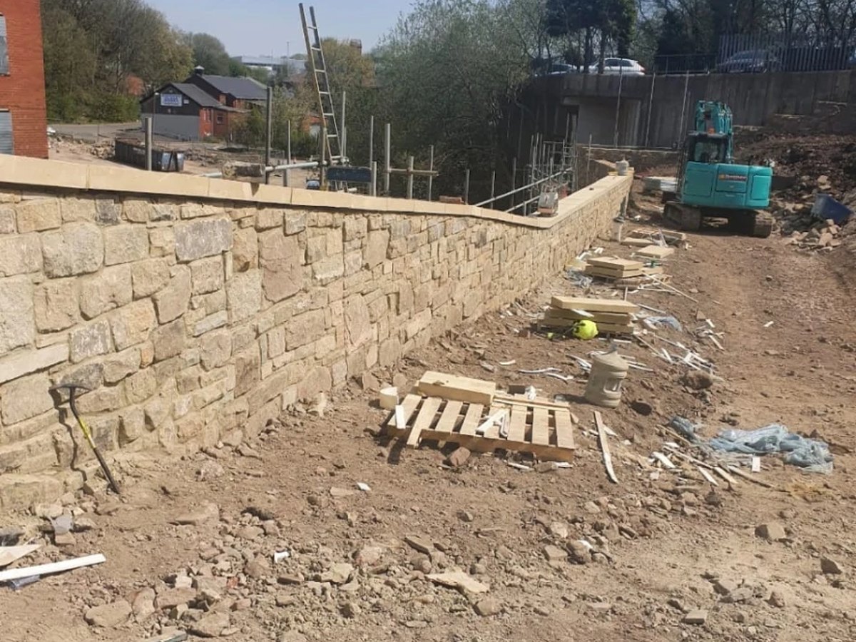Coursed natural stone retaining wall under construction on a sloping site