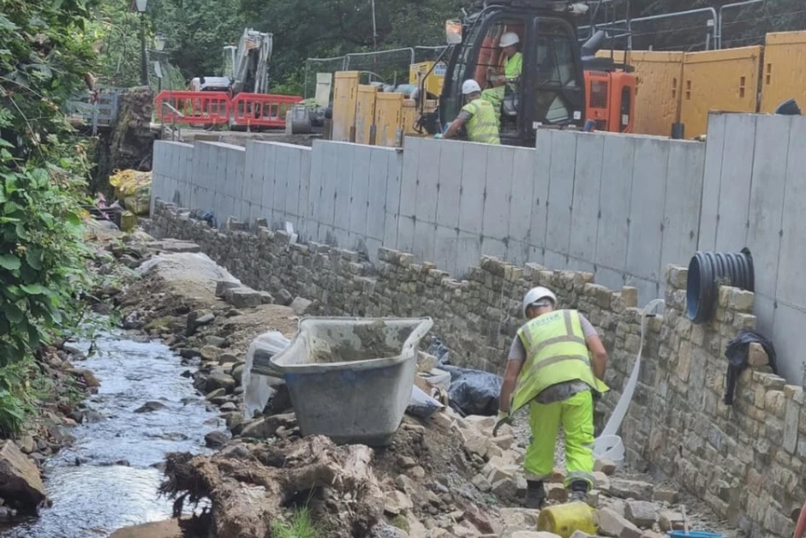 Foster operative building a coursed stone retaining wall alongside a stream